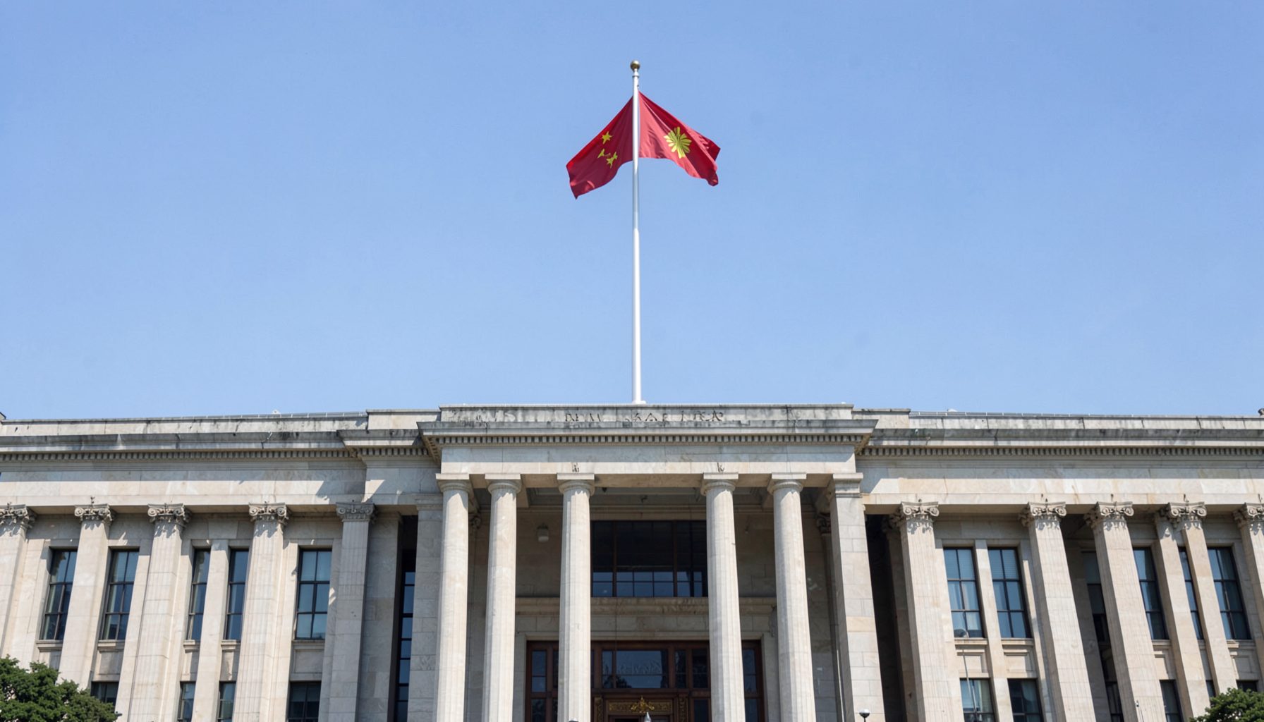 Wide view of a government building facade with a national flag against a clear sky, conveying state and national affairs in a calm, authoritative tone